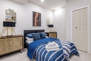A bedroom with a bed, a wardrobe, two bedside tables, a wall-mounted mirror, and a framed picture. - Cozy Luxury Suite With Private Movie Theatre (Calgary)