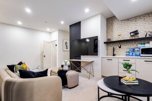 Een moderne woonkamer met een bank, voetenbankje en een ronde tafel met boeken en een plant.