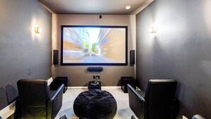 Ein Heimkino mit großer Leinwand, schwarzen Sitzmöbeln und Lautsprechern.