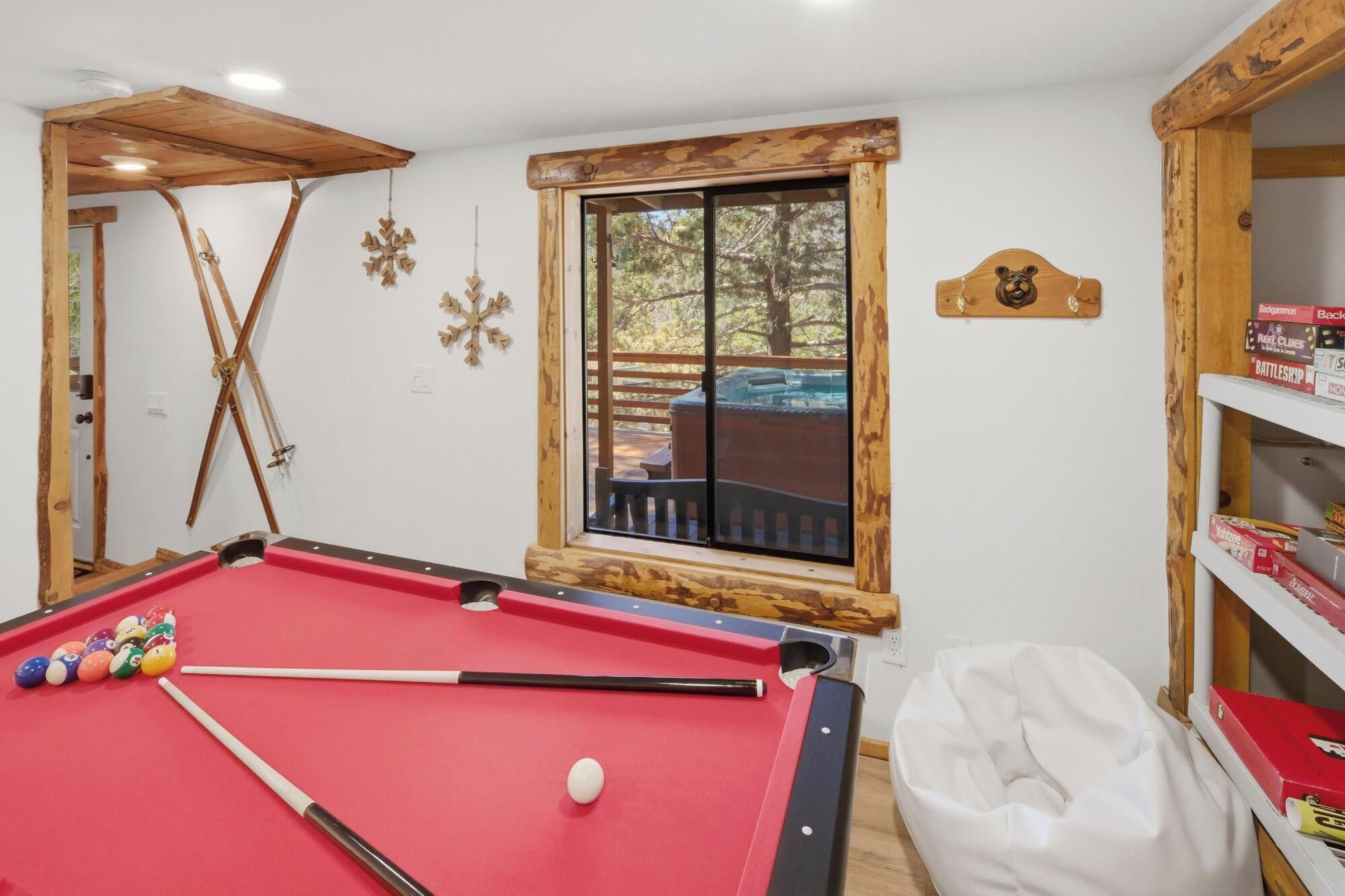 A pool table with balls, a window with a view, and wooden beams.