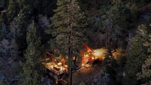 Una cabaña rodeada de un bosque denso con una terraza de madera y zona de estar al aire libre.