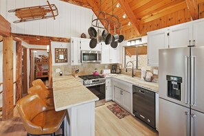 A kitchen with white cabinets, a stove, a microwave, and a refrigerator. - Walk To Bear Mountain, Golf Course or Zoo! PET FRIENDLY! HOT TUB! Fire Pit! Gameroom! (Big Bear Lake)