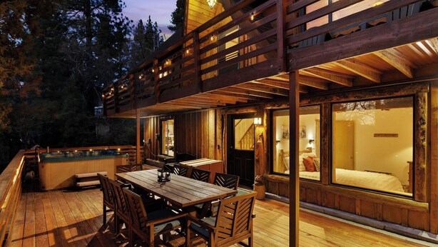 Una cabaña de madera con terraza, jacuzzi y comedor.
