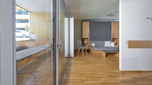 Un interior moderno con suelo de madera, un sofá gris, un armario de madera y un separador de vidrio.