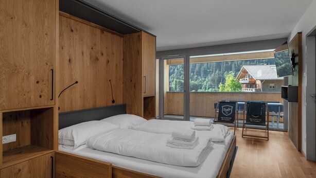 Una habitación moderna con muebles de madera, una cama con ropa de cama blanca, un televisor y vistas a la montaña.
