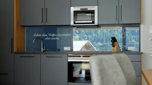 Una cocina moderna con gabinetes grises, horno empotrado y ventana con vista a una casa.