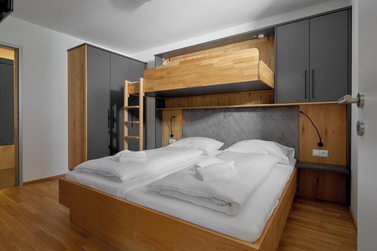 A room with a bunk bed, wooden wardrobe, and a ladder.