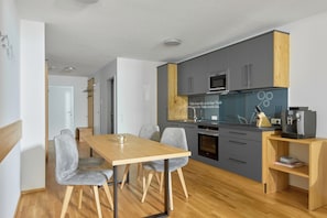 A modern kitchen with grey cabinets, a wooden countertop, and a dining area with a wooden table and grey chairs.
