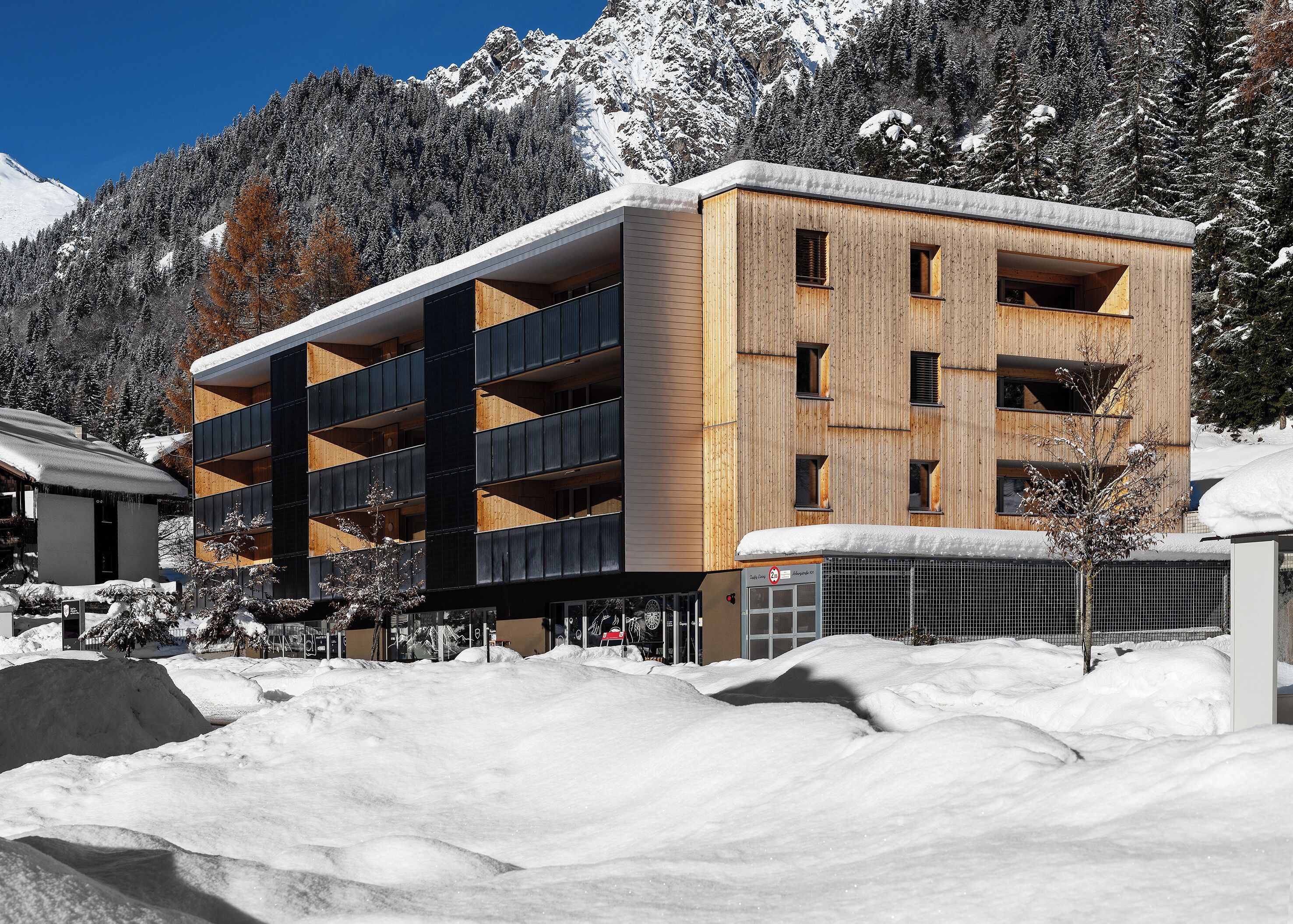 Ein mehrstöckiges Gebäude mit Holzfassade, Balkonen und einem schneebedeckten Berg im Hintergrund.