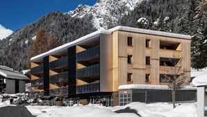 Un edificio de varios pisos con fachada de madera, balcones y una montaña nevada al fondo.