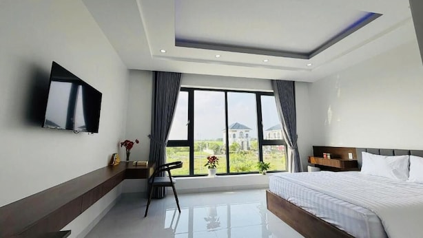 A modern hotel room with a large bed, a TV mounted on the wall, a desk with a chair, and a view of the outside. - Tram Anh 2 Hotel Dong Nai - BAY LUXURY (Nhơn Trạch)