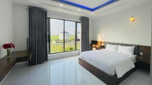A modern hotel room with a large bed, a bedside table, a nightstand, a window with curtains, and a view of the outside. - Tram Anh 2 Hotel Dong Nai - BAY LUXURY (Nhơn Trạch)