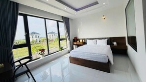 A modern hotel room with a large bed, a TV, a desk, and a window with a view of buildings. - Tram Anh 2 Hotel Dong Nai - BAY LUXURY (Nhơn Trạch)