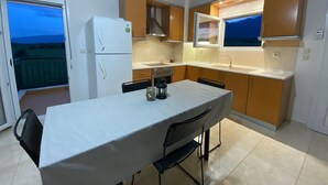 A compact kitchen with a dining table, a refrigerator, and a window overlooking a balcony. - Apartment 'Olyvia' with Sea View, Wi-Fi and Air Conditioning (Plaka Litochorou)
