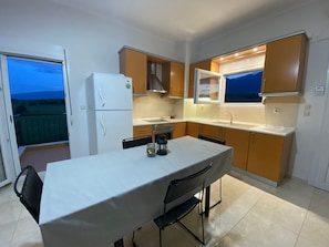 A compact kitchen with a dining table, a refrigerator, and a window overlooking a balcony.