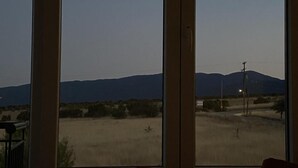 A room with large windows offering a view of a flat landscape with distant hills. - Apartment 'Olyvia' with Sea View, Wi-Fi and Air Conditioning (Plaka Litochorou)