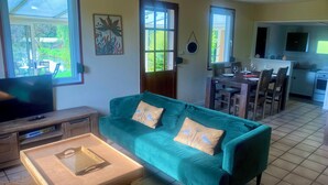 A living room with a sofa, a TV, a coffee table, and a dining area with chairs and a table. - GITE DU MARAIS DE SUZANNE (Suzanne)