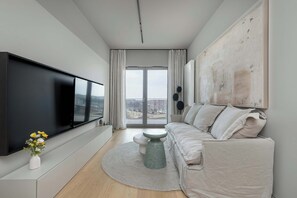A modern living room with a flat-screen TV, a sofa, a round coffee table, and a view of the city through large windows. - Stylish Apartment | Parking, Gym and Cinema in the Building (Katowice)