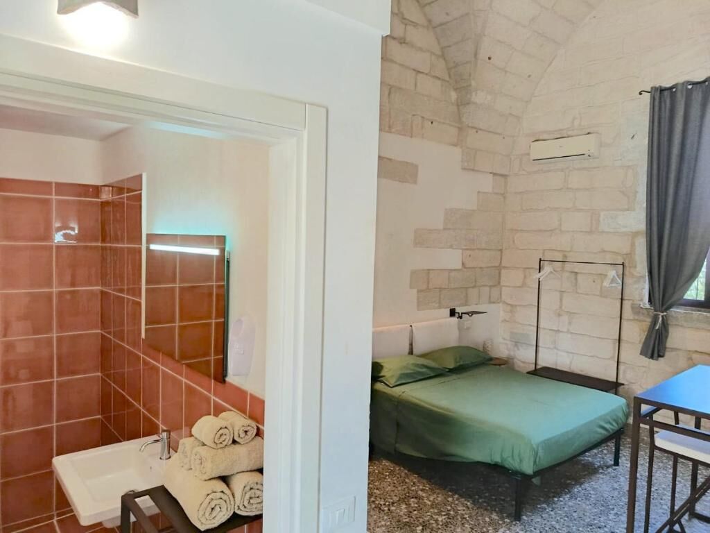 A room with a bed, a table, a window with curtains, and a brick wall.