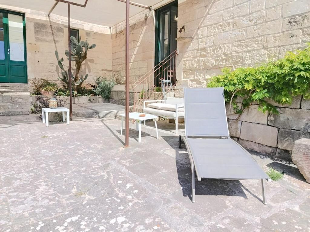 A patio with a metal chair, a white table, and a white lounge chair.