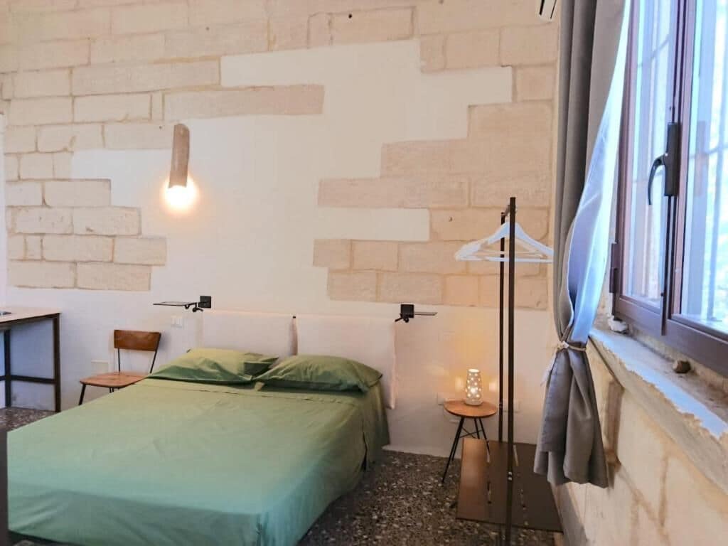 Un dormitorio con cama, escritorio, silla, lámpara colgante y ventana con cortina.