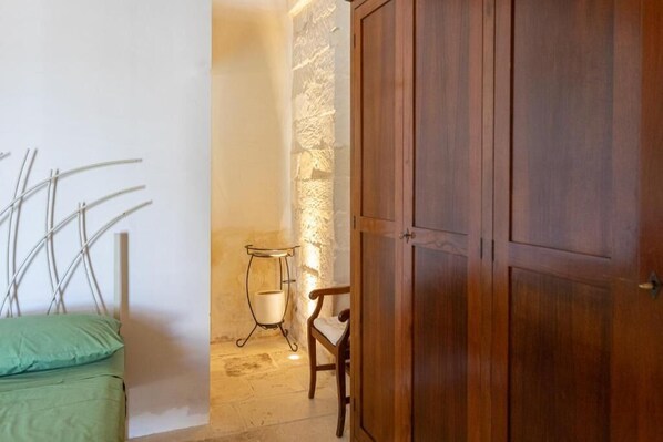 A room with a bed, a wooden wardrobe, a stone wall, and a small table with a chair. - Masseria Torre Sant'Andrea (Borgagne)