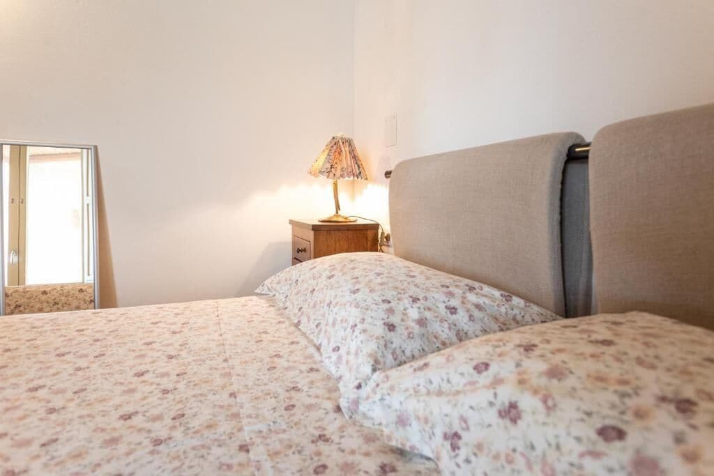 A bedroom with a bed, a nightstand, a lamp, and a mirror.