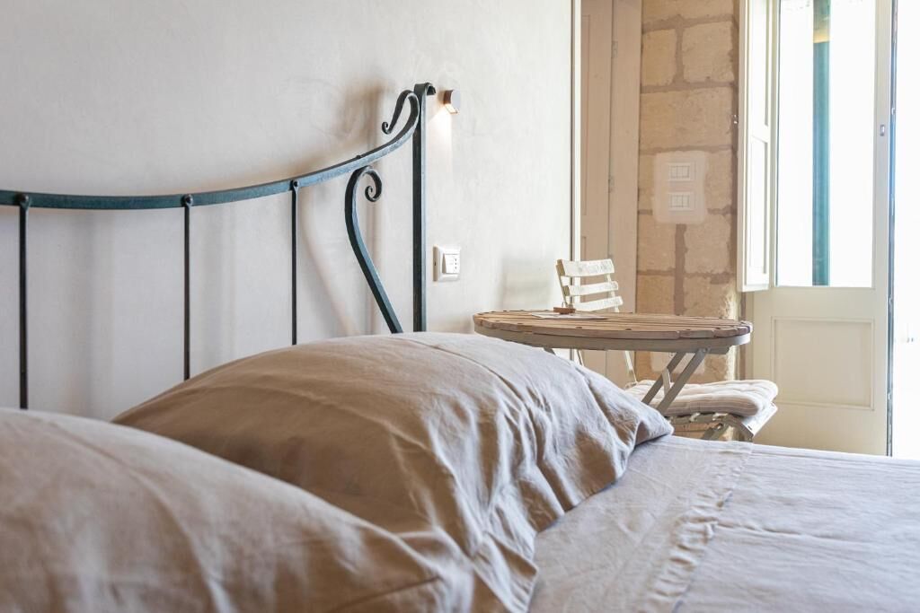 Un lit avec une tête de lit en métal, une petite table en bois et un mur en pierre.