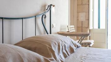 Un lit avec une tête de lit en métal, une petite table en bois et un mur en pierre.