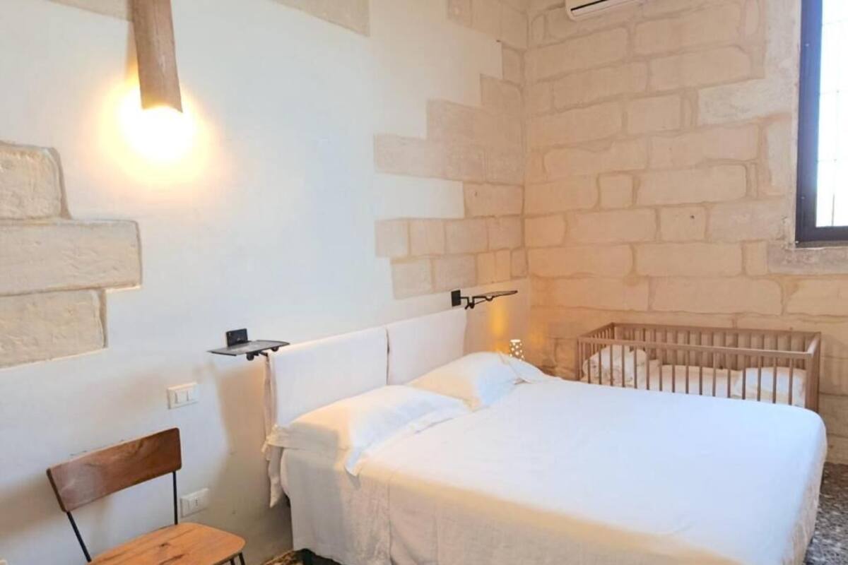 A bedroom with a bed, a crib, a chair, and a wall-mounted shelf.