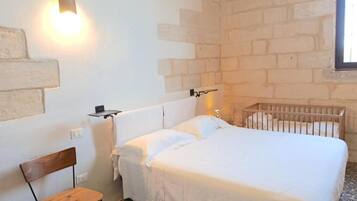 Een slaapkamer met een bed, een ledikantje, een stoel en een wandplank.