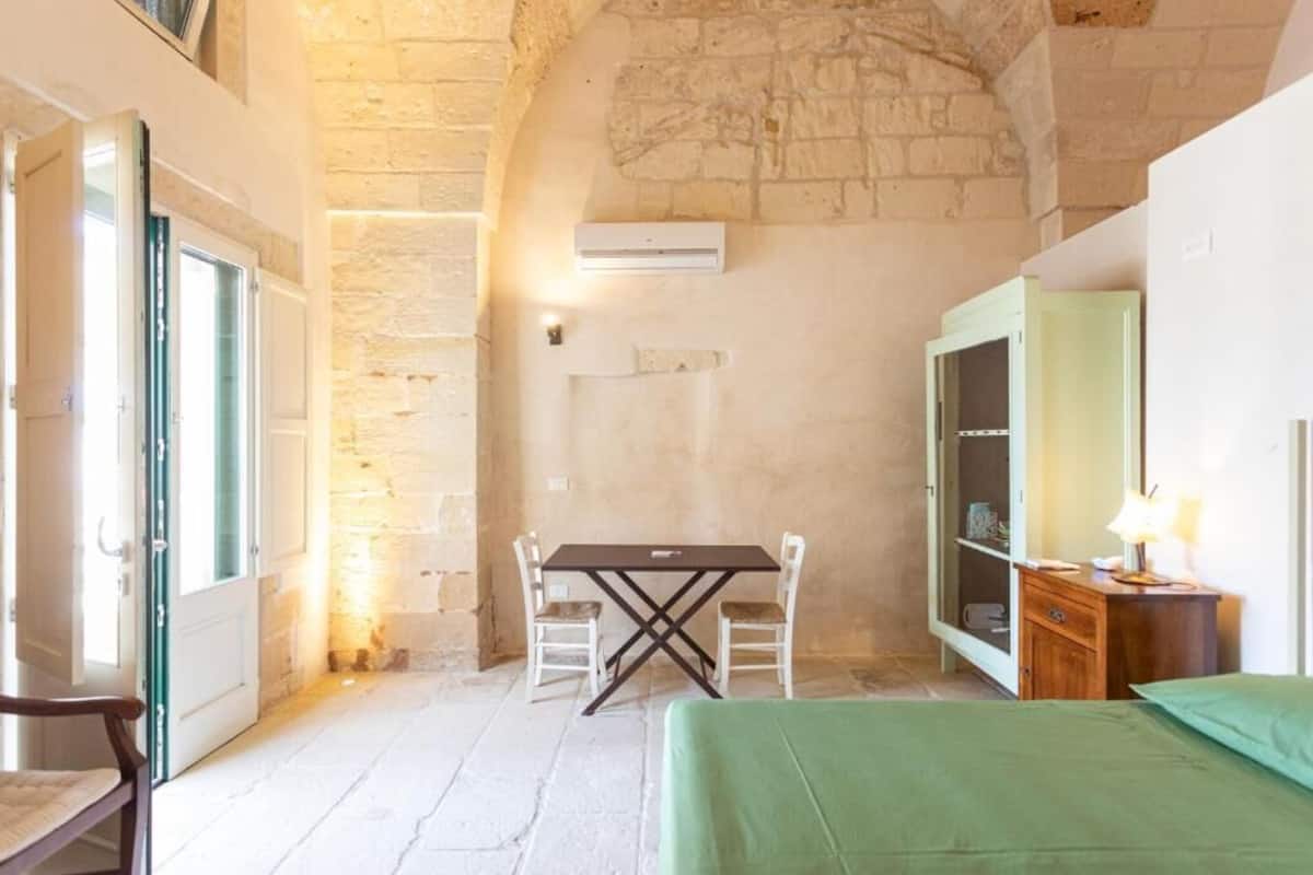 A room with a stone wall, a bed, a table with chairs, and a wardrobe.