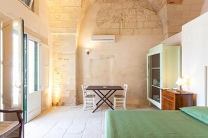 Una habitación con pared de piedra, una cama, una mesa con sillas y un armario.