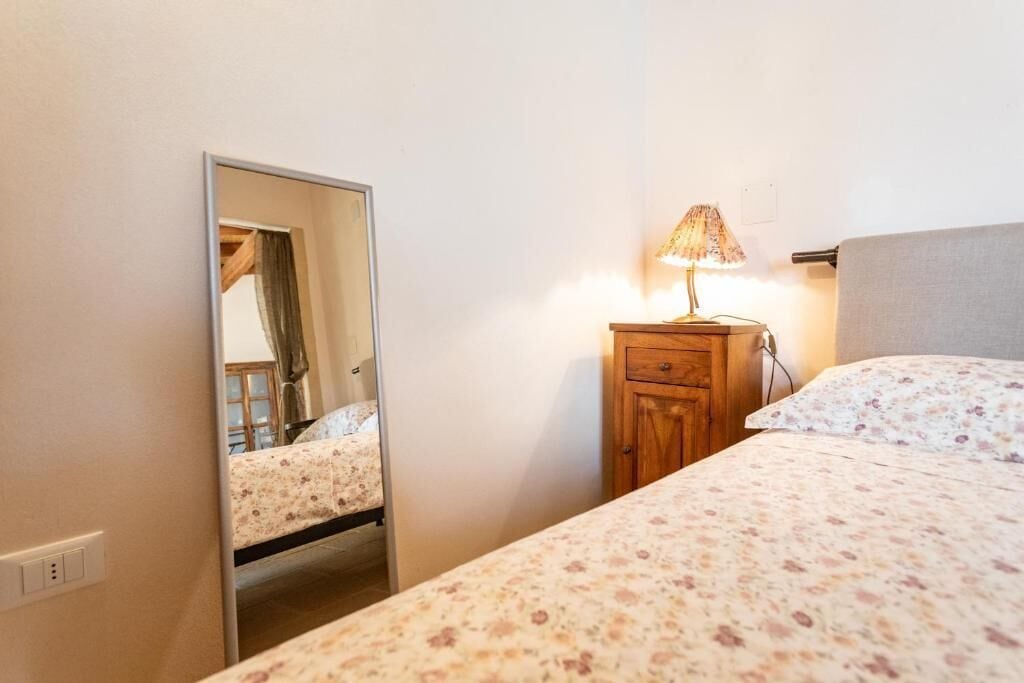 A bedroom with a bed, a nightstand with a lamp, a mirror, and a wooden cabinet.