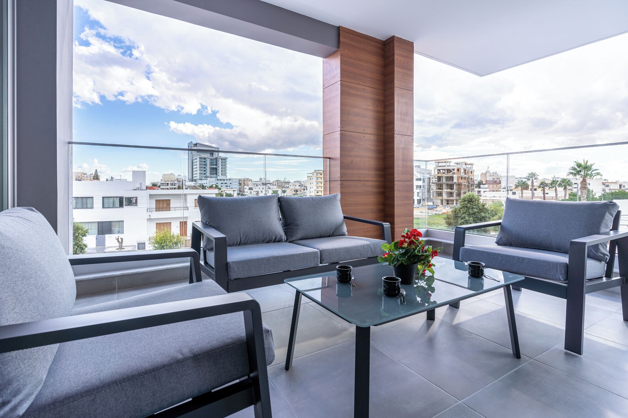 A balcony with a sofa, chairs, and a glass table.