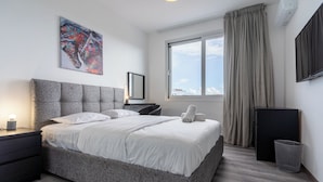 A modern hotel room with a large bed, a desk, a chair, a TV, and a window with curtains. - Sunflower 1-BR Apt. & Balcony in Larnaca (Larnaca)