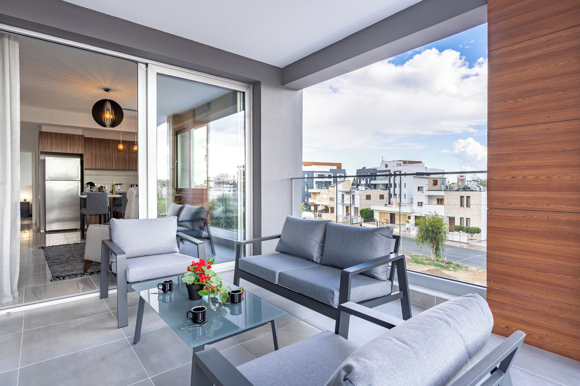 Ein modernes Wohnzimmer mit einem Glastisch, grauen Sofas und Blick auf die Stadt durch große Fenster.