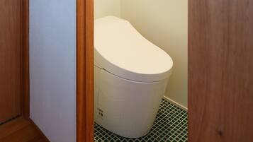 Ein kleines, schmales Badezimmer mit einer weißen Toilette, einem hölzernen Türrahmen und einem grün gefliesten Boden.