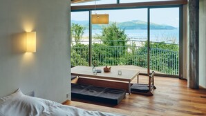 Ein Schlafzimmer mit Holzboden, einem Bett, einem Tisch mit Lampe und einem Balkon mit Meerblick.