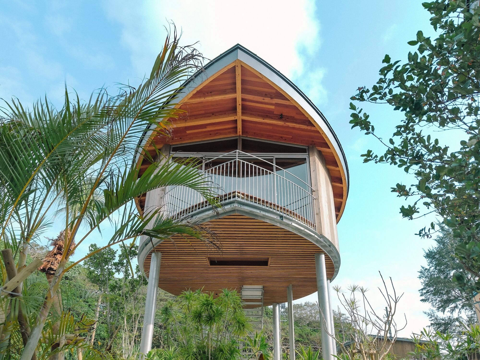 A wooden structure with a balcony, surrounded by tropical vegetation.
