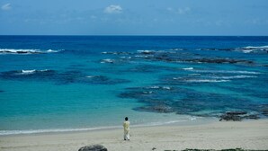 Ein Strand mit klarem, blauem Wasser und einer Person, die im Sand steht.