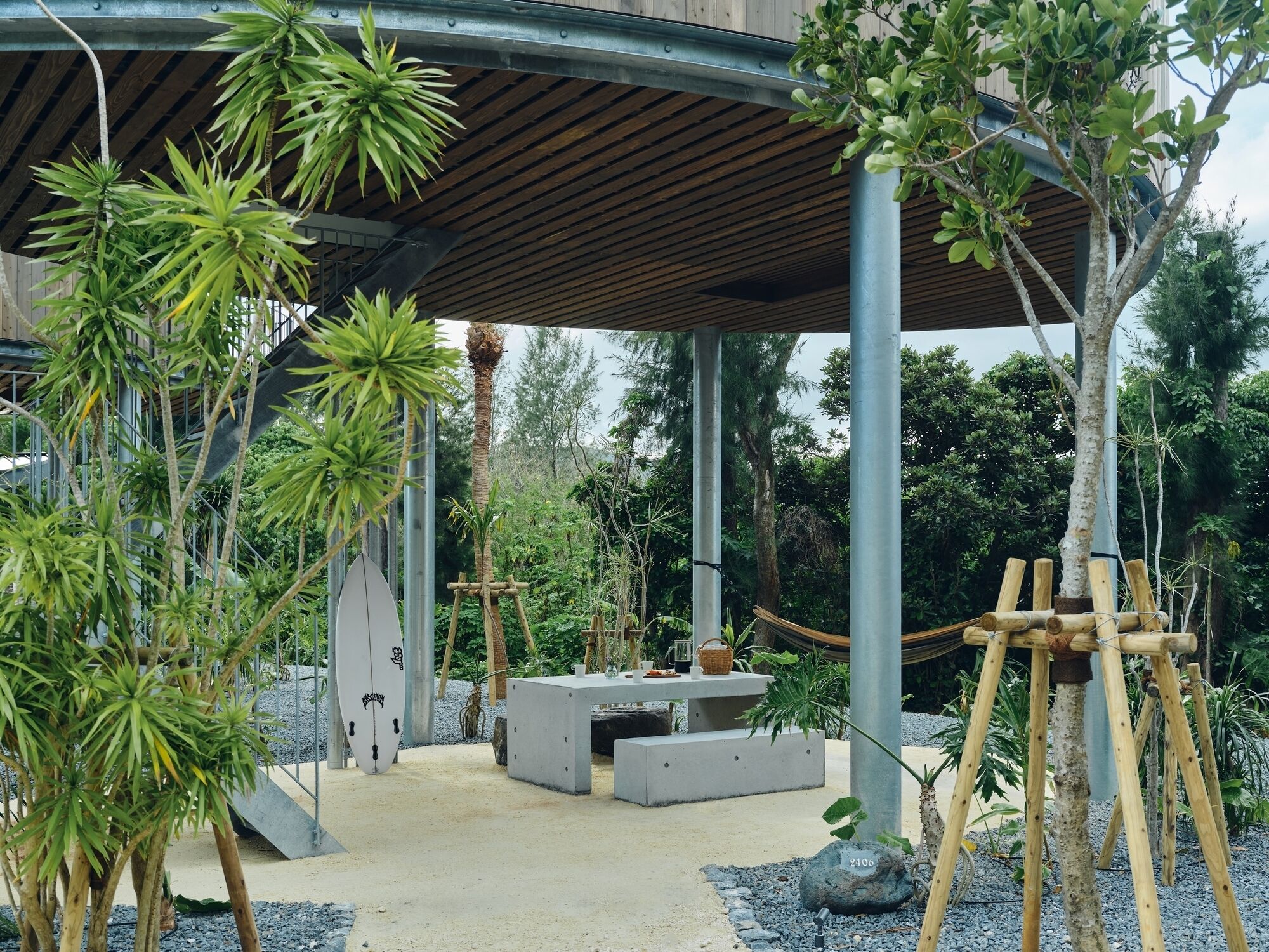 A covered outdoor area with a concrete table, seating, and a variety of plants.