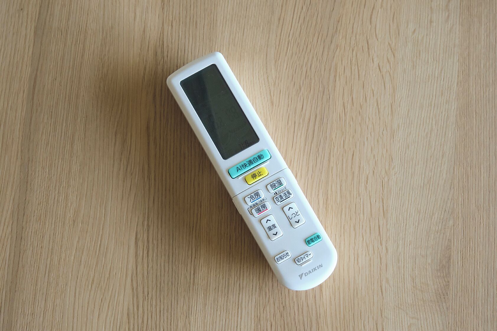 Un termómetro digital blanco con pantalla y varios botones sobre una superficie de madera.