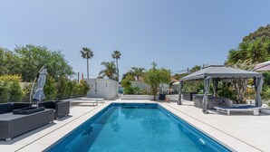 A rectangular swimming pool with tiled edges, surrounded by lounge chairs and a covered seating area. - Guesthouse 'Casa Caro' with Mountain Views, Wi-Fi, and Air Conditioning (Estepona)