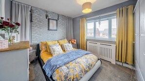 Un dormitorio con cama, mesita de noche, lámpara, cortinas y una ventana.