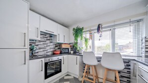 Una cocina moderna con armarios blancos, un horno negro, un microondas y una ventana con persianas.