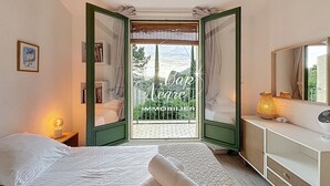 Een slaapkamer met twee bedden, een nachtkastje met een lamp, een dressoir en een raam met uitzicht op groen.