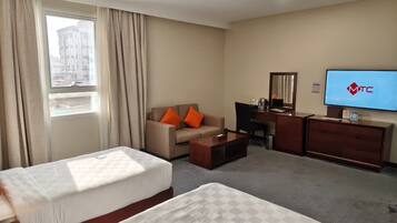 A hotel room with two beds, a sofa, a desk, a TV, and a window with curtains.