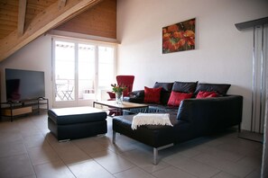 Ein Wohnzimmer mit einer schwarzen Couch, roten Kissen, einem Couchtisch, einem Fernseher und einem Bild an der Wand.