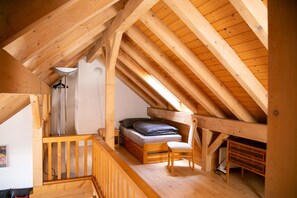 Ein Schlafzimmer im Dachgeschoss mit Holzboden, einem Bett, einem Sessel, einem Schreibtisch und einer Lampe.